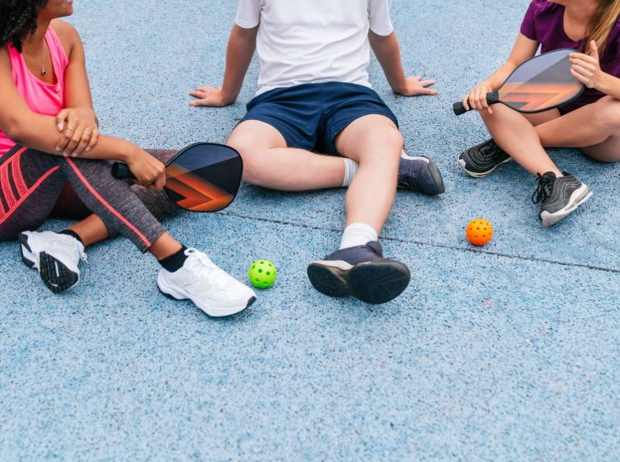 Drei Pickleball-Spieler sitzen auf dem Platz, halten ihre Paddel und genießen eine Pause nach einem spannenden Spiel